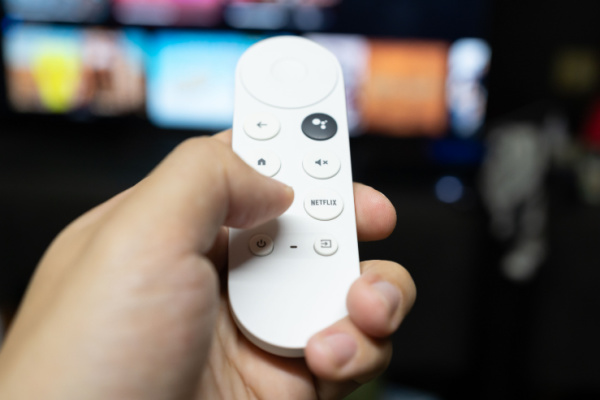 A person holding a Google Chromecast remote and pointing it to a TV screen.